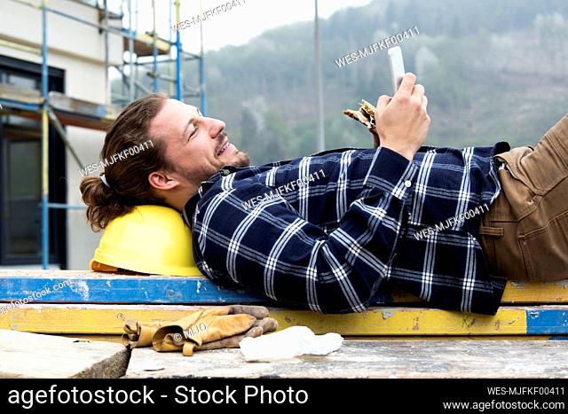 Construction worker using smart phone while eating food on wood at construction site