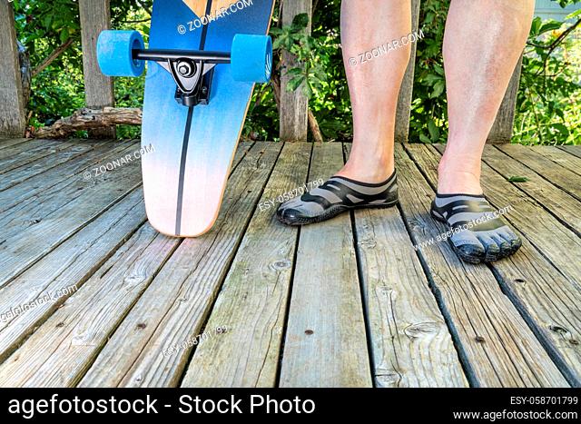Legs of mature male with a cruising longboard on a wooden patio, recreation concept