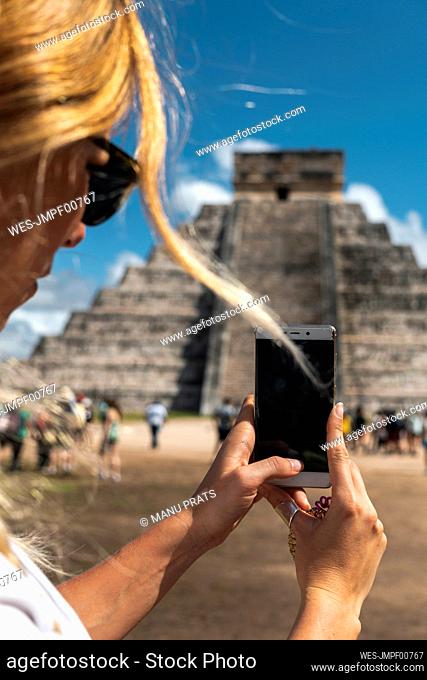 Mexico, Yucatan, Chichen Itza, Hands of female tourist taking smart phone photos of Temple Of Kukulcan
