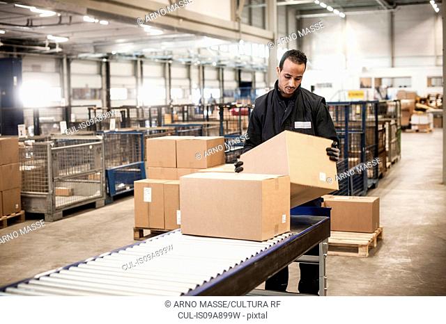 Male warehouse worker checking cardboard box from conveyor belt