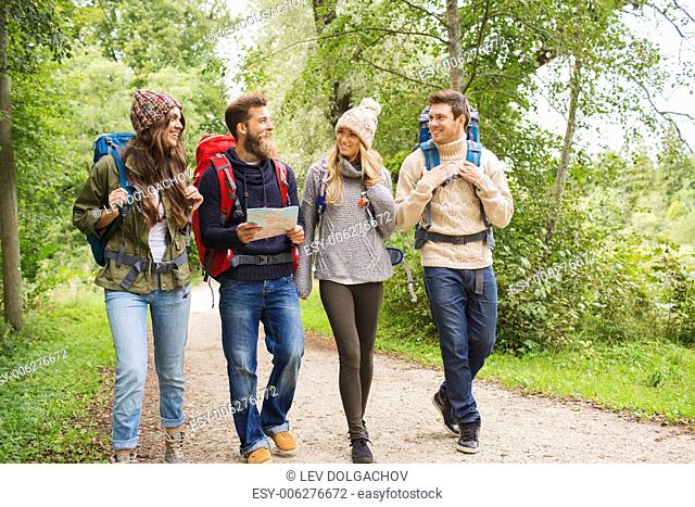adventure, travel, tourism, hike and people concept - group of smiling friends walking with backpacks and map walking outdoors