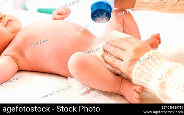 Closeup of mother applying talcum powder while changing messy diapers of her little baby son on changing table. Concept of babies and newborn hygiene and...