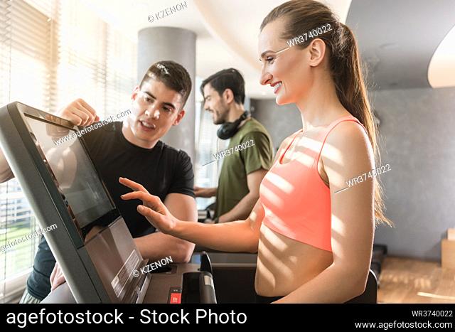 Motivated young woman increasing the speed of the treadmill during a workout session supervised by a professional personal trainer