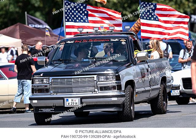 dpatop - 20 July 2019, Lower Saxony, Hanover: Visitors drive their pickups with US flags across the grounds during the Street Mag Show in Hanover