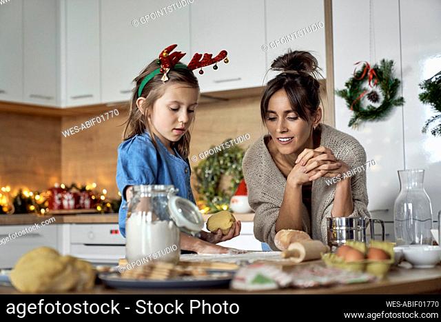 Girl making cookie dough standing by mother in kitchen