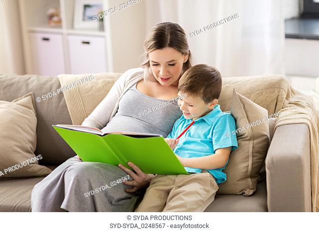 pregnant mother and little son with book at home