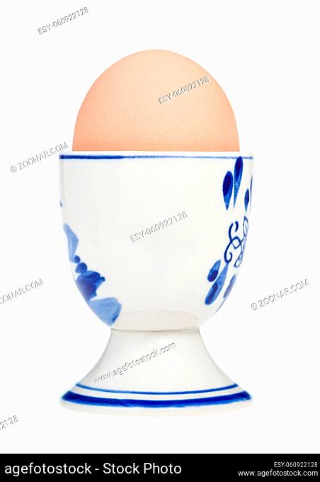 side view of brown boiled egg in ceramic egg cup with a blunt end up isolated on white background