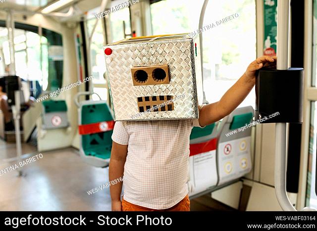 Boy wearing robot mask made of box standing in train