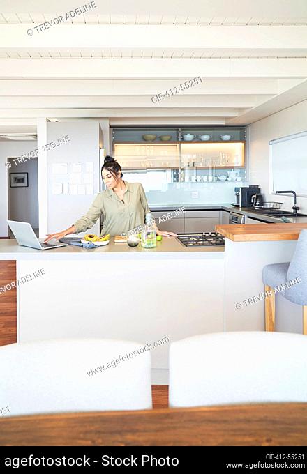 Woman with laptop working and cooking in modern kitchen