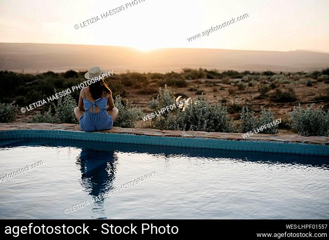 Woman looking at sunset sitting on poolside