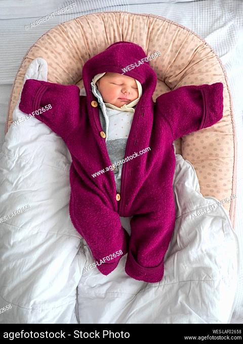 Cute baby girl in warm clothing sleeping on bed at home