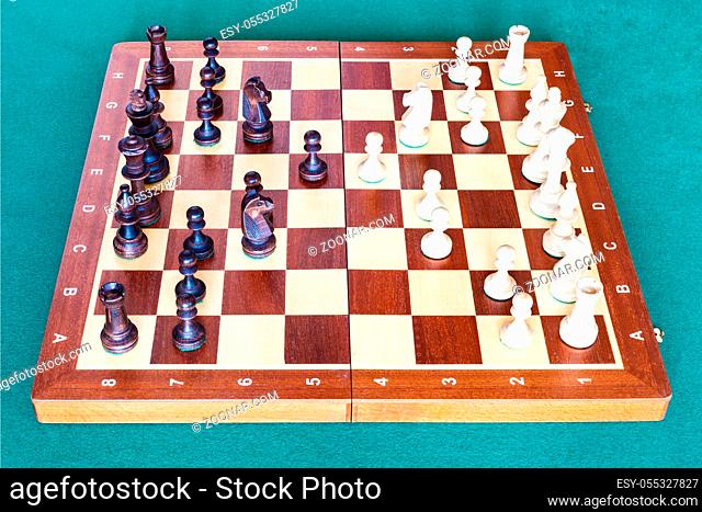 side view of chess gameplay on wooden chessboard on green baize table