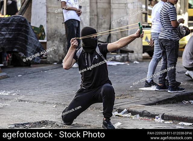 28 September 2022, Palestinian Territories, Hebron: A Palestinian protester uses a sling shot during clashes with Israeli Defence Forces in the West Bank city...