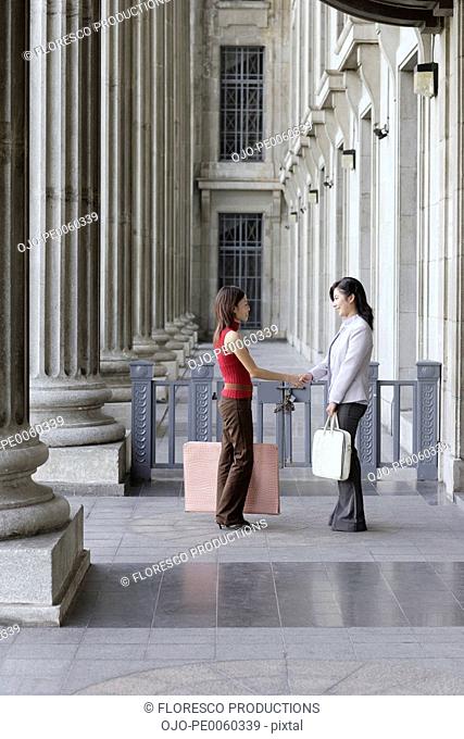 Two businesswomen outdoors by building shaking hands
