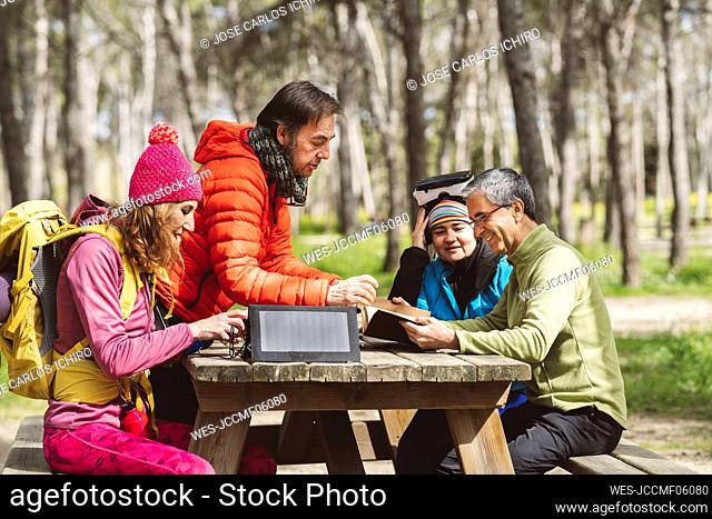 Mature men discussing over diary with women sitting at picnic table in forest