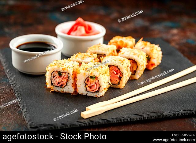 Japanese sushi rolls served on stone slate on dark background. Sushi rolls, maki, pickled ginger and soy sauce. Sushi background