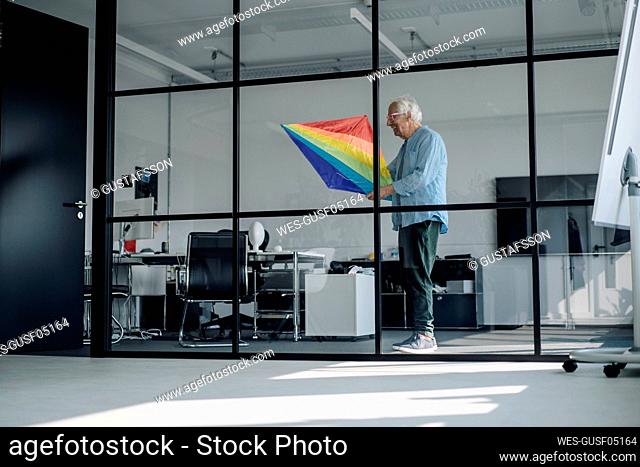 Businessman holding multi colored kite while standing in office