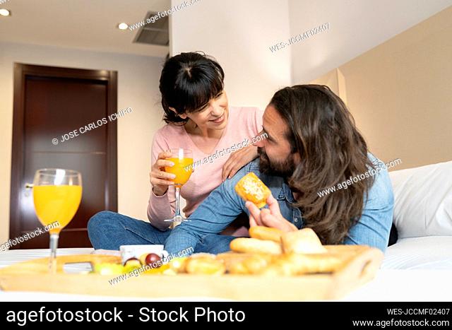 Smiling couple looking at each other while having breakfast on bed at hotel suite