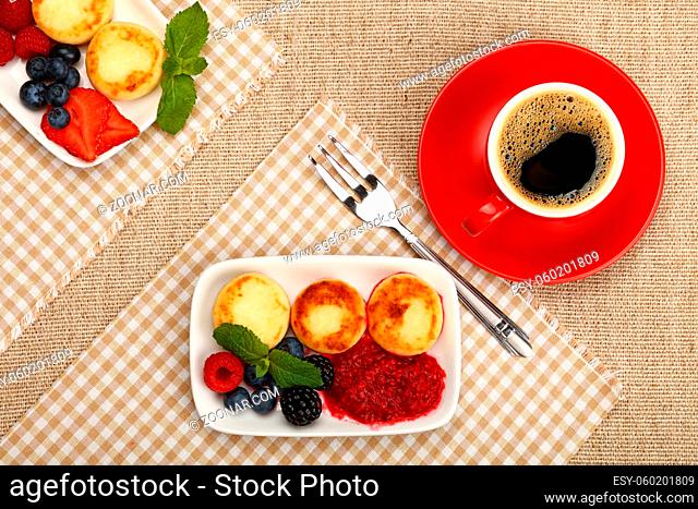 Close up serving portion of European quark cheese pancakes dessert with fruits and cup of black coffee, elevated top view, directly above