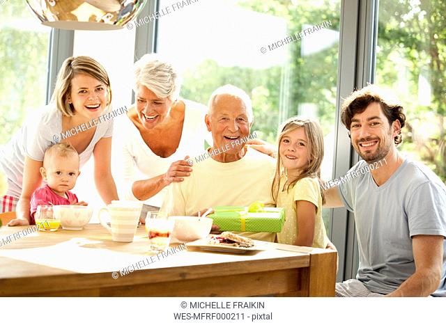 Portrait of happy extended family with present at breakfast table