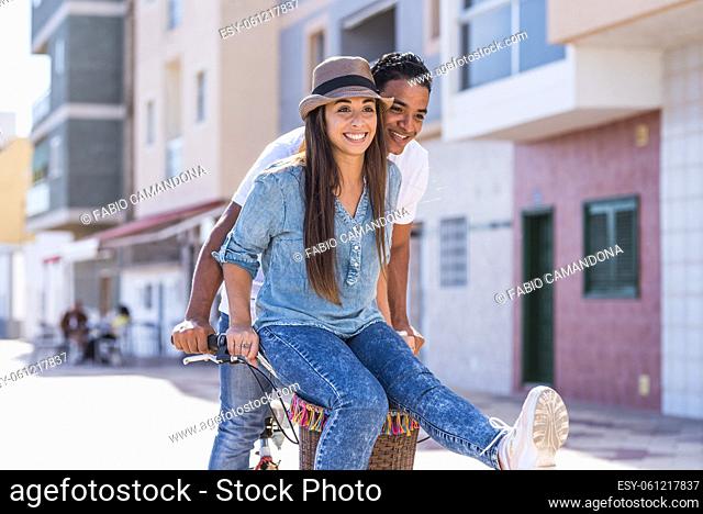 Interracial couple have fun together riding a bike in outdoor in the city - happiness and joy young people interracial boyfriend and girlfriend - two enjoy...