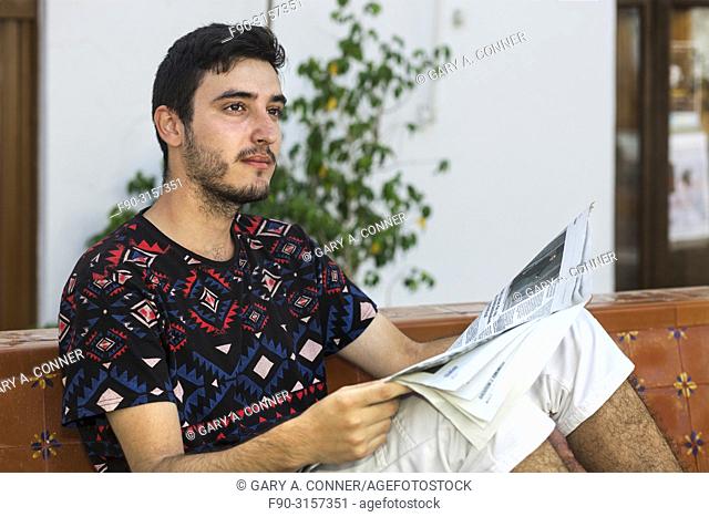 Young man reads newspaper at outdoor cafe, Salobreña, Spain