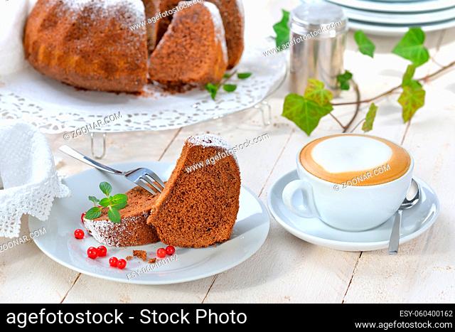 Schoko-Guglhupf mit Zartbitterschokolade mit einer Tasse Cappuccino serviert - Freshly baked ring-shaped cake with chocolate
