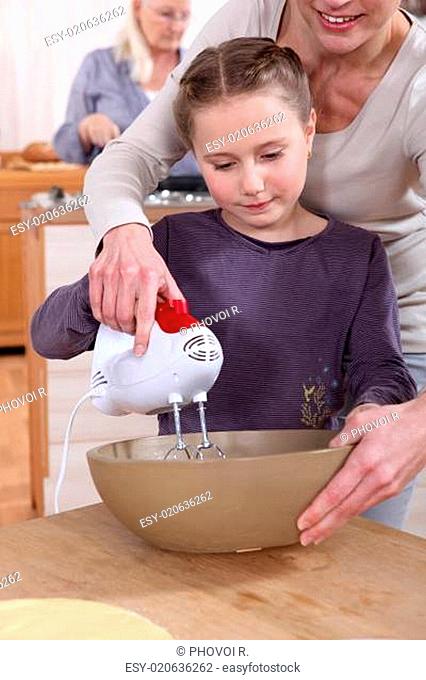Woman helping her daughter use a hand mixer