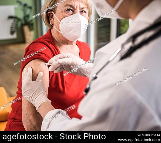 Senior woman with face mask getting vaccinated at home