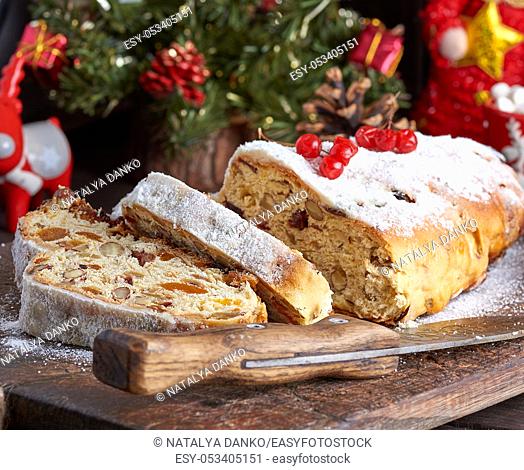 Stollen a traditional European cake with nuts and candied fruit, is dusted with icing sugar and cut into pieces on a brown wooden board