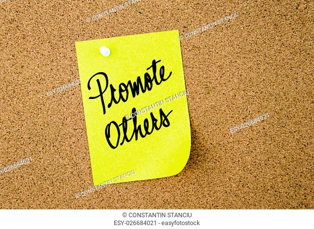 Promote Others written on yellow paper note pinned on cork board with white thumbtacks, copy space available