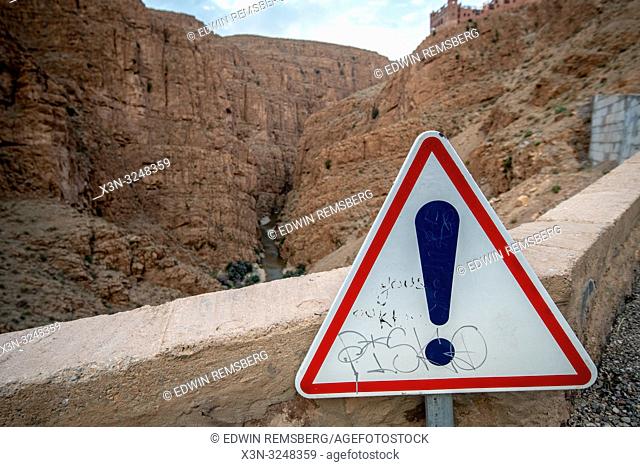 A graffitied warning sign near a cliff edge, Atlas mountains,