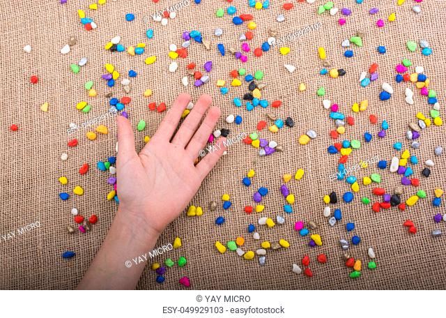 Hand placed on colorful pebbles on canvas background