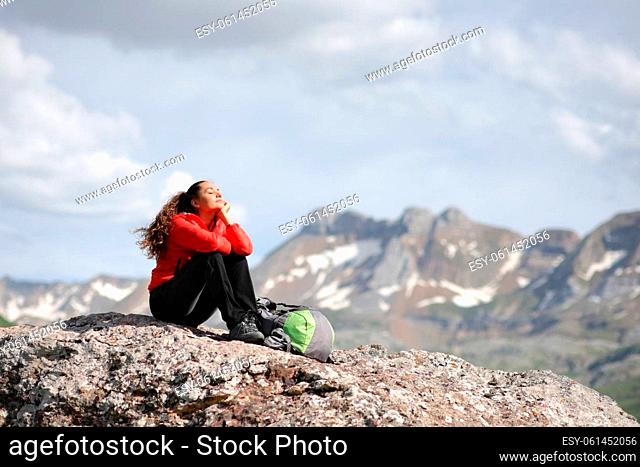 Hiker in red resting alone meditating sitting in the top of a high mountain
