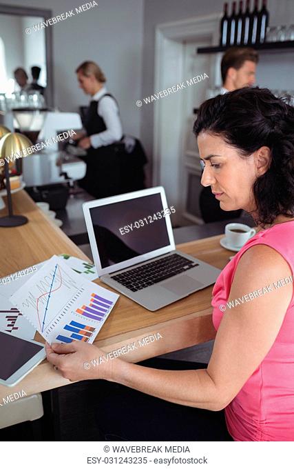 Woman reading graph chart and working with laptop at bar counter