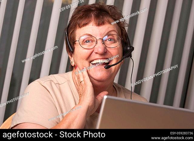 Smiling Senior Adult Woman with Telephone Headset In Front of Computer Monitor