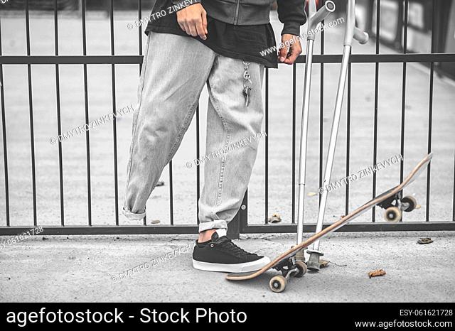 Balance. Leg of guy with disability skillfully stepping on skateboard and acceptance crutches near gate of skatepark, no face