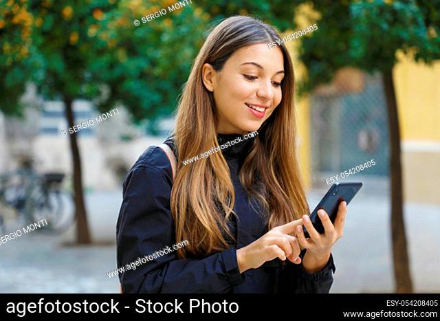 Portrait of a beautiful smiling woman using a mobile phone in city street with tangerines trees on the background