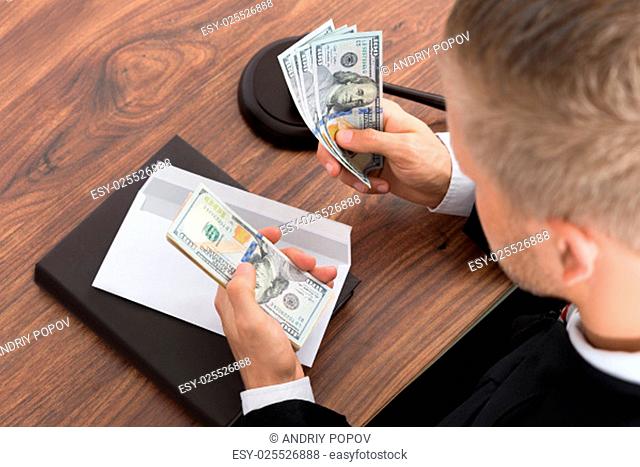 Close-up Of Judge Counting Money At Desk In Courtroom