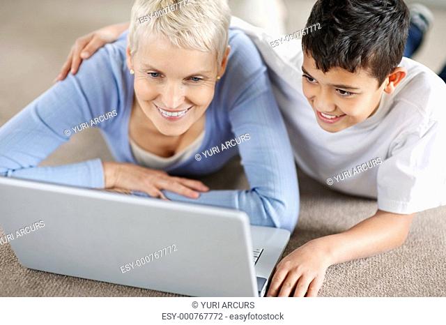 Grandson and grandmother lying on floor and smiling in front of laptop
