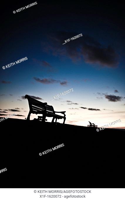 Silhouettes of empty park benches against a twilight sky, UK
