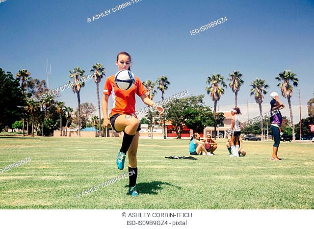 Teenage schoolgirl soccer player practicing keepy uppy on school sports field