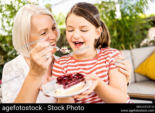 Grandmother feeding cake to granddaughter at balcony