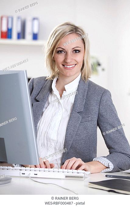 Germany, Bavaria, Munich, Businesswoman using computer in office, smiling, portrait