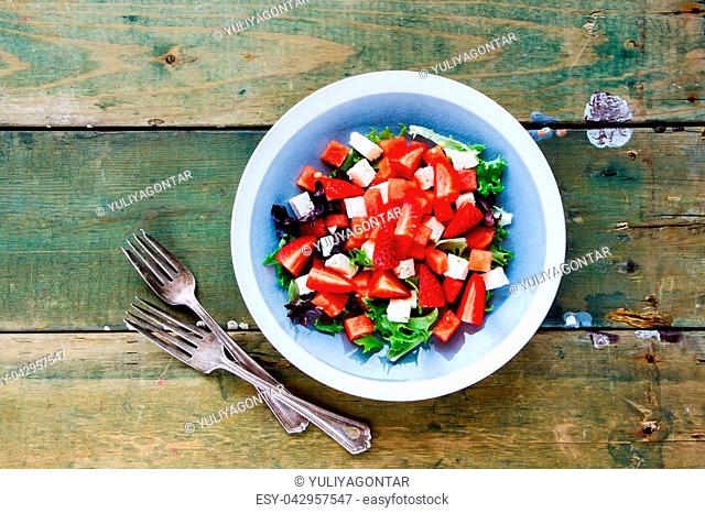 Healthy summer watermelon feta salad with arugula and fresh strawberry on wooden background. Flat lay, top view