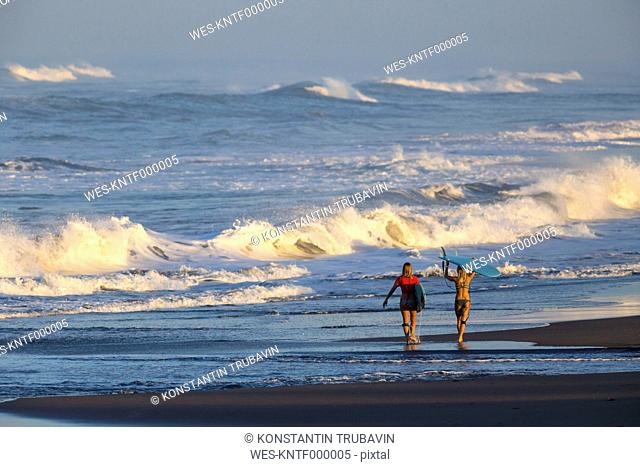 Indonesia, Bali, two women carrying surfboards at seafront