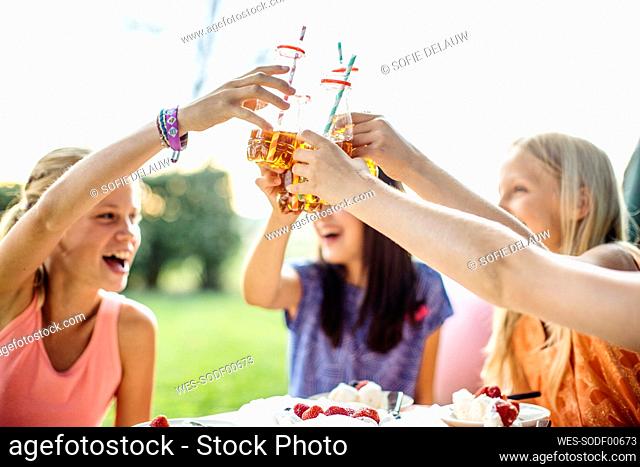 Happy girls clinking bottles on a birthday party outdoors
