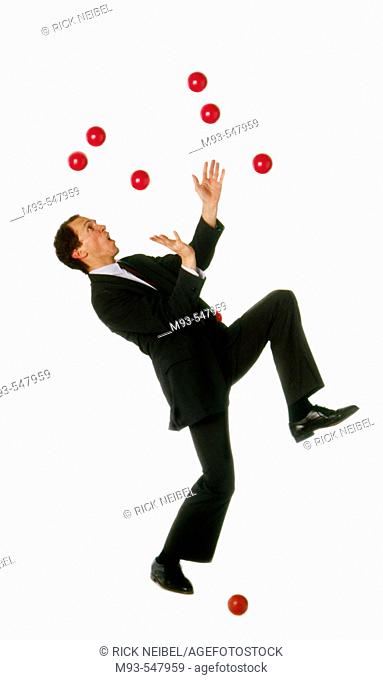 Business man struggling unsuccessfully to juggle multiple red balls; one already on ground