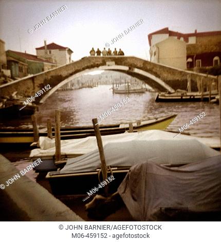 Six men sitting in a row on a bridge in Murano, Italy