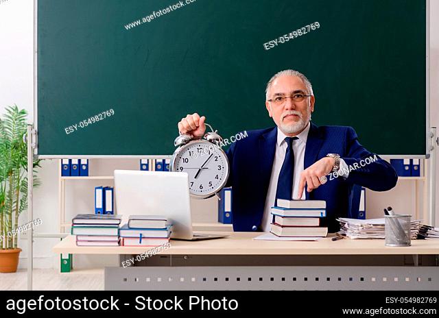 Aged male teacher in front of chalkboard